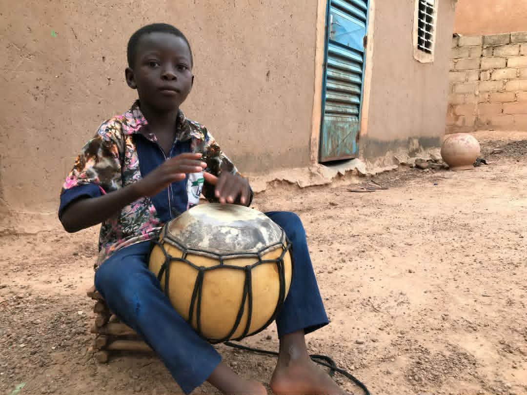 A boy in Ouagadougou playing a traditional drum with a gourd body